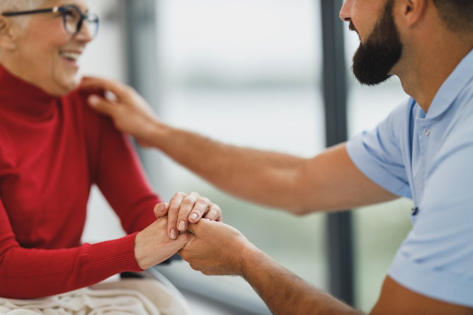 Caregiver gently holding the hand of a smiling senior woman at home